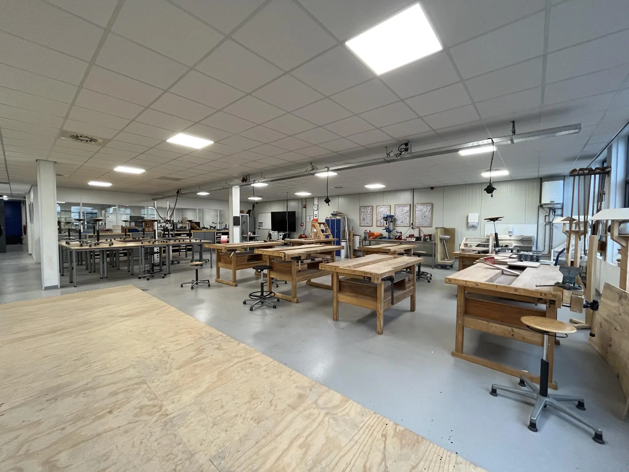 Ruime en goed verlichte werkplaats aan de Niels Bohrweg met houten werkbanken en diverse gereedschappen.